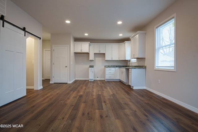 kitchen featuring sink, dark wood-type flooring, dark stone countertops, white cabinets, and a barn door