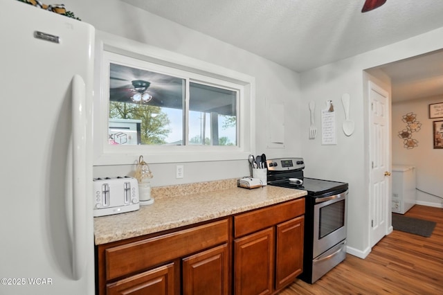 kitchen featuring freestanding refrigerator, stainless steel range with electric stovetop, light wood-type flooring, and ceiling fan