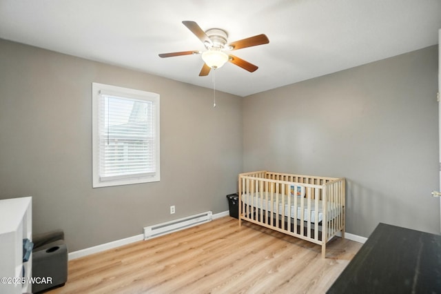 bedroom featuring a baseboard heating unit, baseboards, a crib, and wood finished floors