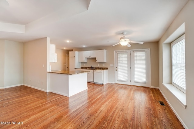 kitchen with visible vents, light wood-style flooring, white cabinets, white dishwasher, and baseboards