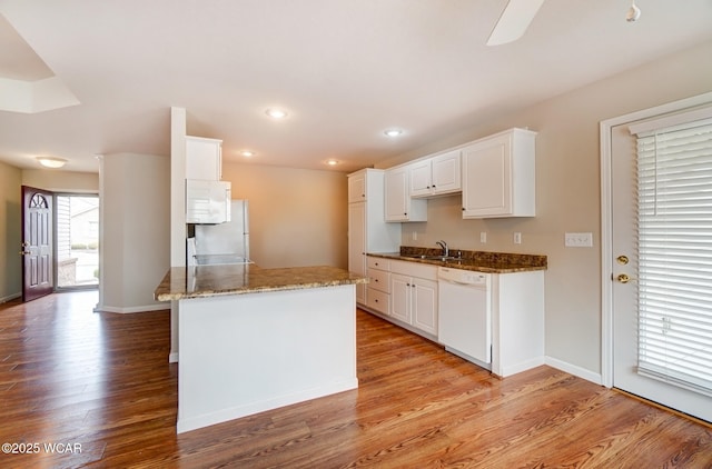 kitchen featuring white cabinets, a sink, dark stone countertops, light wood-type flooring, and white appliances