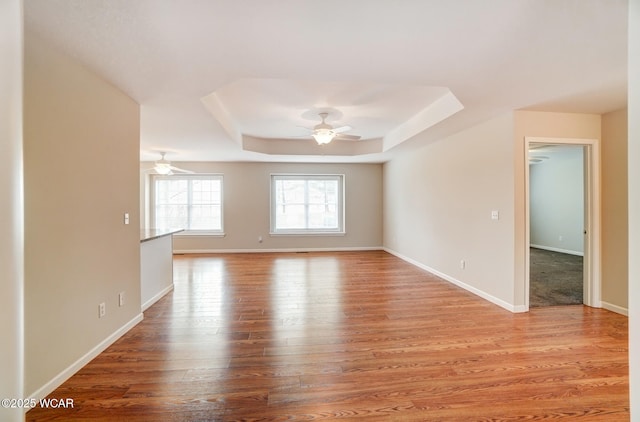 empty room featuring light wood finished floors, baseboards, a tray ceiling, and ceiling fan