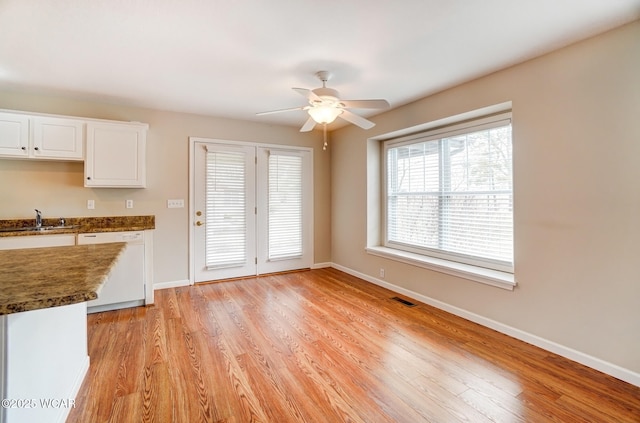 unfurnished dining area featuring light wood-style flooring, baseboards, ceiling fan, and a sink