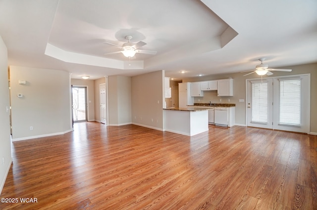 unfurnished living room featuring light wood-style floors, a tray ceiling, and ceiling fan