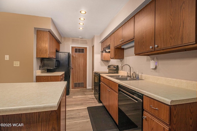 kitchen featuring visible vents, under cabinet range hood, light countertops, black appliances, and a sink