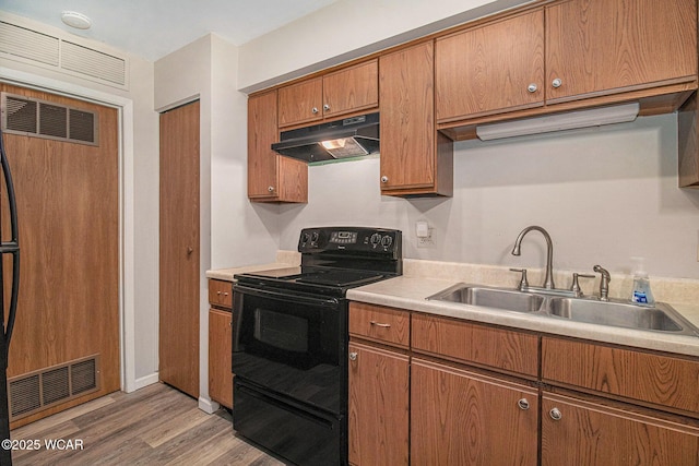 kitchen with light countertops, a sink, paneled built in refrigerator, under cabinet range hood, and black / electric stove