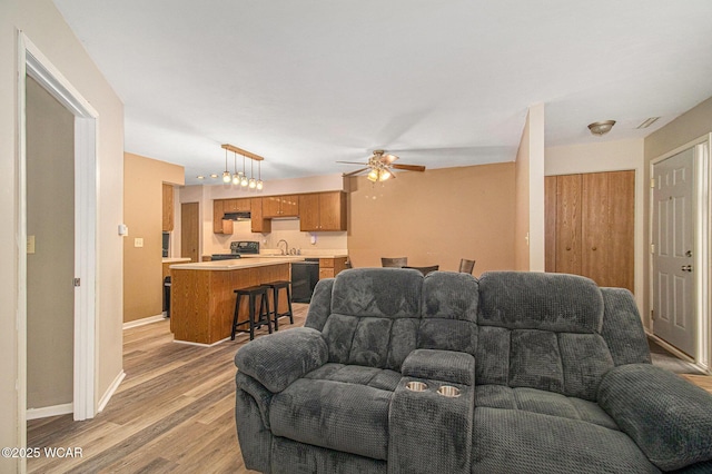 living room featuring a ceiling fan, light wood-type flooring, visible vents, and baseboards