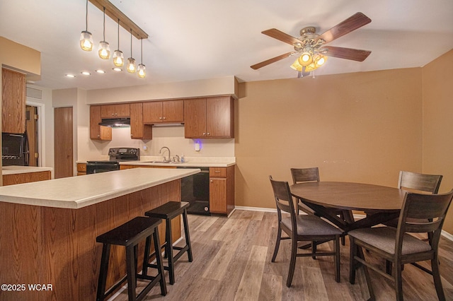 kitchen with brown cabinetry, a sink, under cabinet range hood, and black appliances