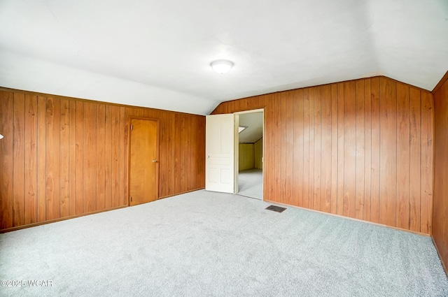 carpeted empty room with lofted ceiling and wooden walls