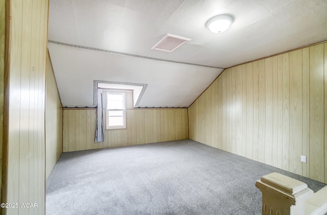 bonus room featuring lofted ceiling, light colored carpet, a textured ceiling, and wood walls