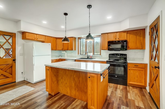 kitchen featuring sink, hanging light fixtures, a center island, black appliances, and light hardwood / wood-style flooring