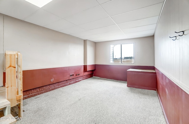 spare room with a paneled ceiling, carpet, and wood walls