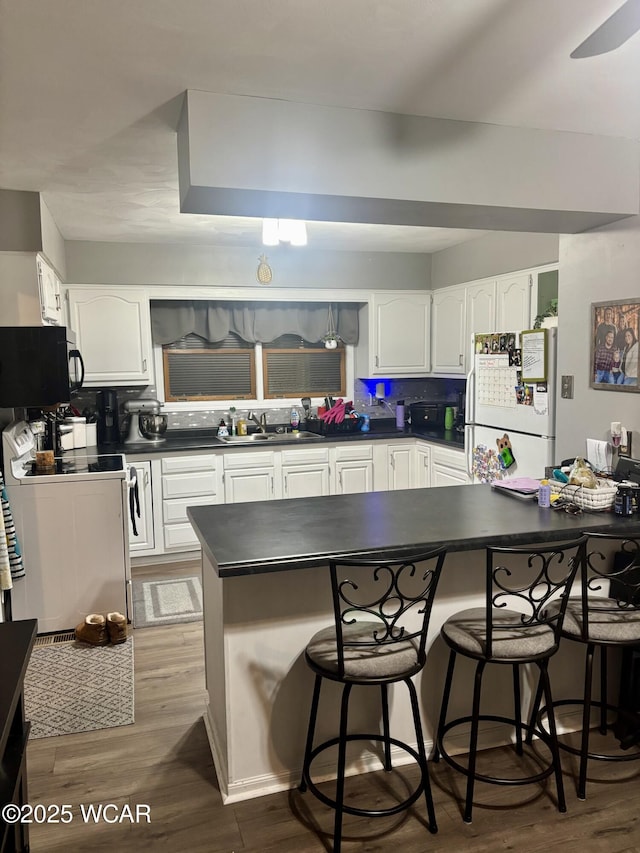 kitchen featuring hardwood / wood-style floors, white cabinets, a kitchen bar, kitchen peninsula, and white appliances