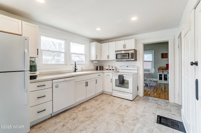 kitchen featuring white appliances, visible vents, a sink, light countertops, and white cabinetry