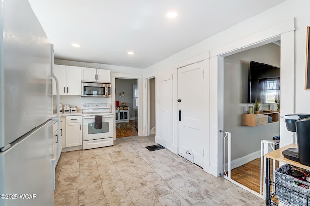 kitchen with white electric range, stainless steel microwave, white cabinetry, freestanding refrigerator, and light countertops