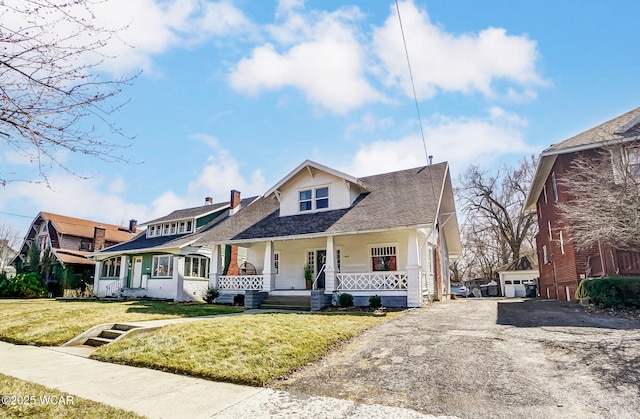 view of front of house with an outdoor structure, a detached garage, covered porch, and a front yard