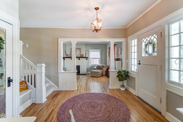 foyer entrance featuring stairway, baseboards, light wood finished floors, a fireplace, and ornamental molding