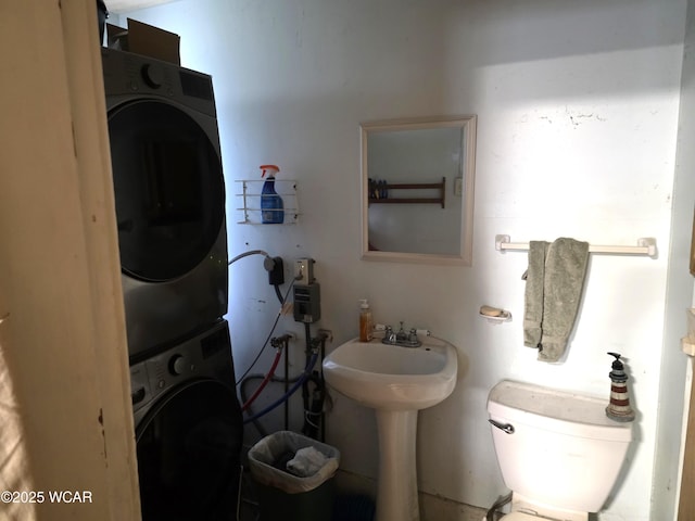 half bathroom with toilet, stacked washer and dryer, and a sink