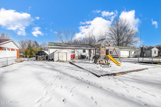 snow covered house with a trampoline, a playground, and a storage unit