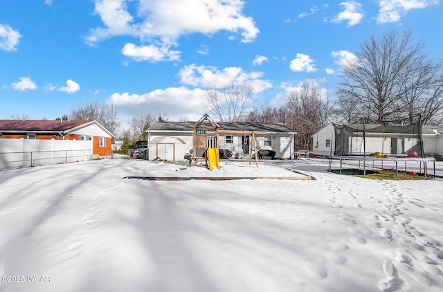 snow covered rear of property with a trampoline, a playground, and a shed