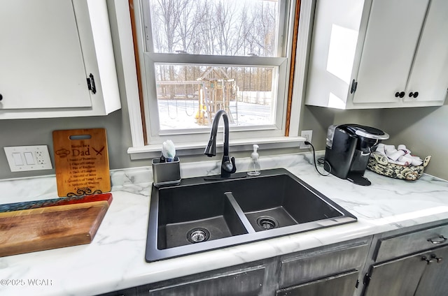 kitchen featuring light stone countertops, sink, and white cabinets