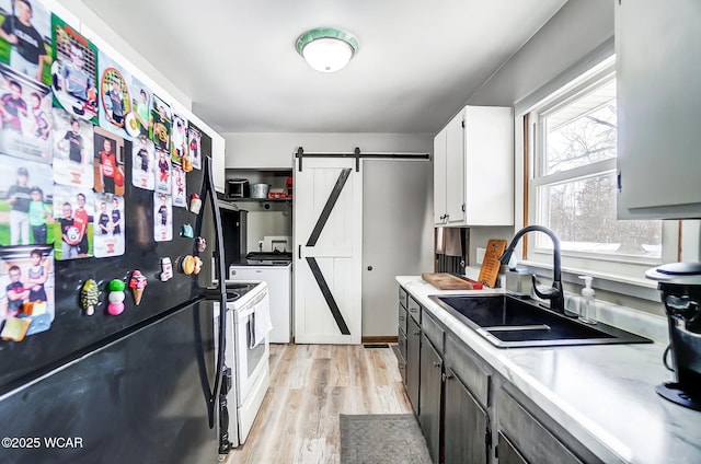 kitchen featuring white electric stove, sink, white cabinets, black fridge, and a barn door