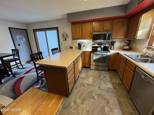 kitchen with appliances with stainless steel finishes, brown cabinets, a peninsula, light countertops, and a sink