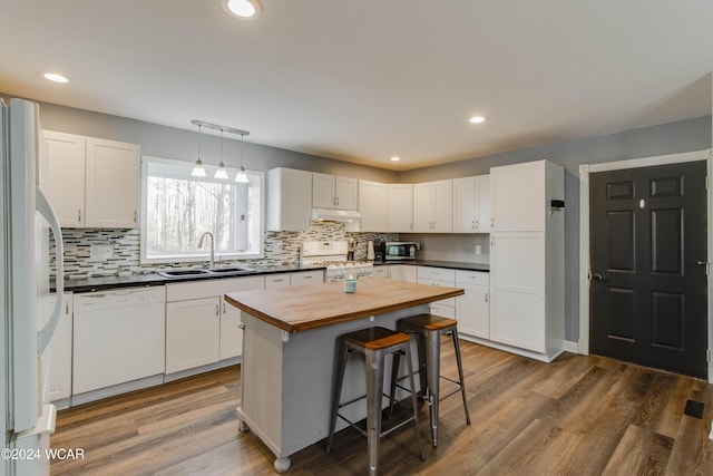 kitchen featuring a kitchen island, sink, white cabinets, a kitchen bar, and white appliances