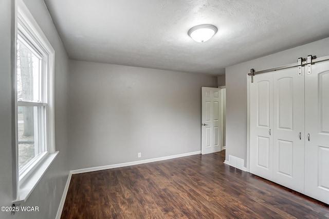 unfurnished bedroom featuring a barn door, dark hardwood / wood-style flooring, a closet, and a textured ceiling