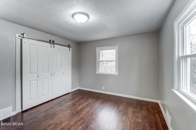 unfurnished bedroom with dark wood-type flooring, a barn door, a closet, and a textured ceiling