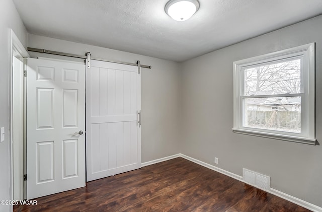 unfurnished bedroom with dark wood-type flooring, a barn door, and a textured ceiling