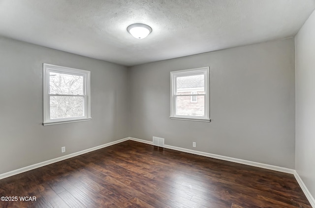 empty room featuring plenty of natural light, a textured ceiling, and dark hardwood / wood-style flooring