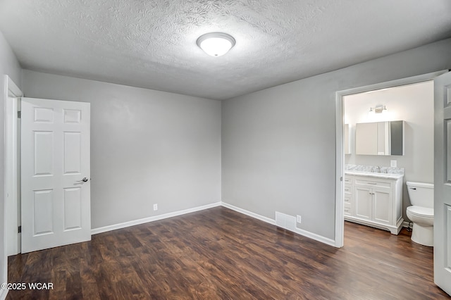 unfurnished bedroom with ensuite bathroom, dark hardwood / wood-style floors, sink, and a textured ceiling