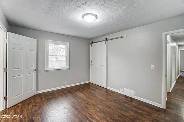 unfurnished bedroom with a barn door, a textured ceiling, and dark hardwood / wood-style flooring