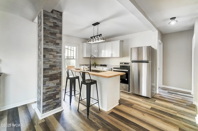 kitchen featuring wood finished floors, wooden counters, a sink, appliances with stainless steel finishes, and a kitchen bar