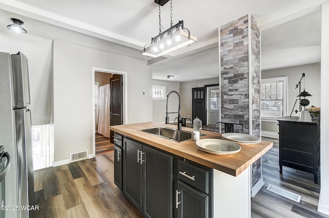 kitchen with visible vents, butcher block counters, freestanding refrigerator, and a sink