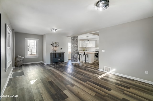 unfurnished living room featuring visible vents, baseboards, dark wood-style flooring, an inviting chandelier, and a sink