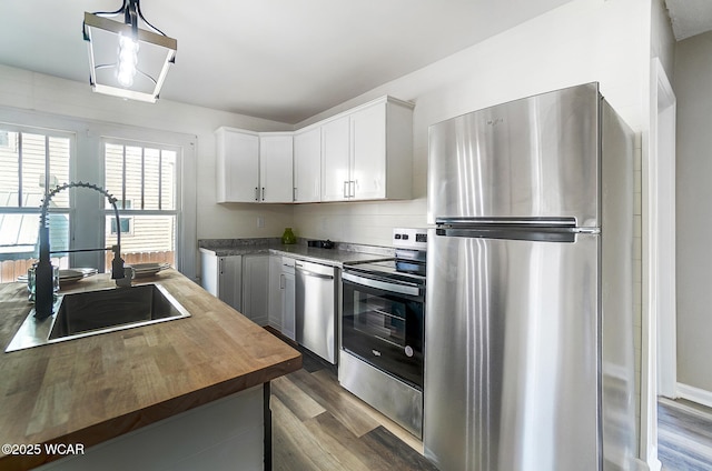 kitchen with dark wood finished floors, a sink, appliances with stainless steel finishes, white cabinetry, and butcher block counters