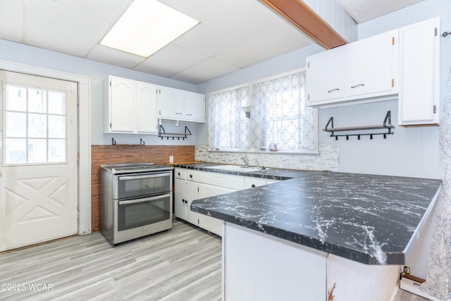 kitchen with dark countertops, double oven range, a peninsula, light wood-style floors, and white cabinets