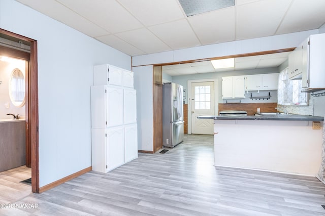 kitchen with light wood-type flooring, a peninsula, white cabinetry, dark countertops, and stainless steel fridge