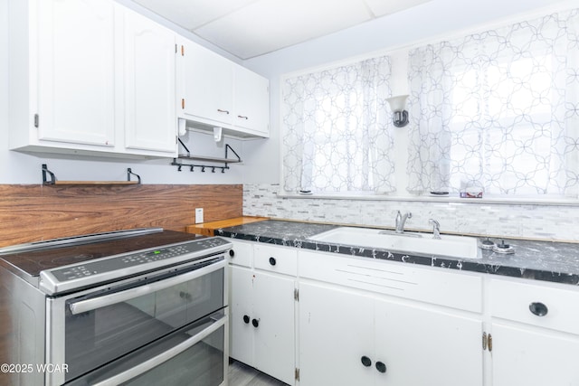 kitchen featuring range with two ovens, white cabinets, dark stone countertops, and a sink