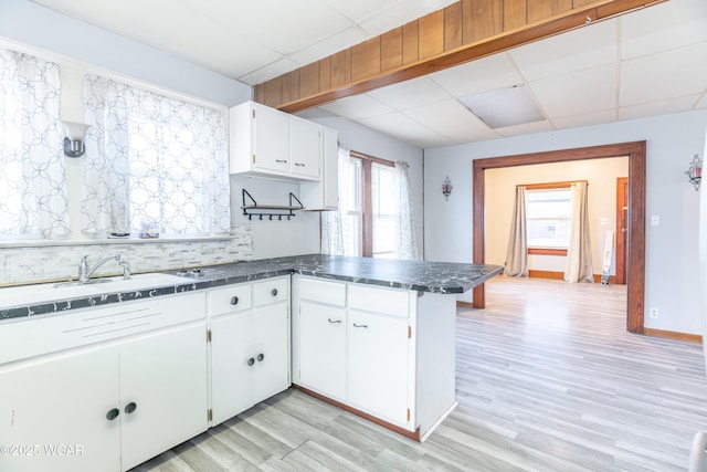 kitchen with decorative backsplash, a peninsula, a paneled ceiling, and light wood finished floors