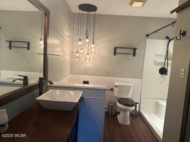 bathroom with hardwood / wood-style floors, a shower, tile walls, vanity, and toilet