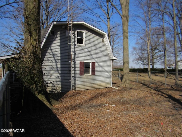 view of side of home with fence and a gambrel roof