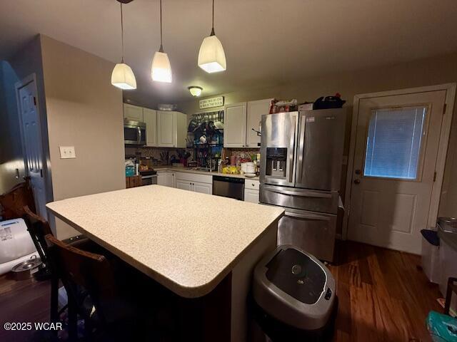 kitchen featuring white cabinetry, a center island, hanging light fixtures, appliances with stainless steel finishes, and a kitchen breakfast bar