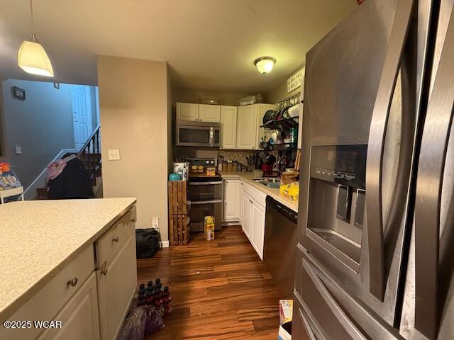 kitchen with dark wood-type flooring, sink, white cabinetry, hanging light fixtures, and stainless steel appliances