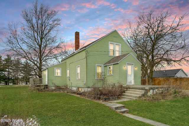 back of property at dusk featuring a lawn, a chimney, and fence