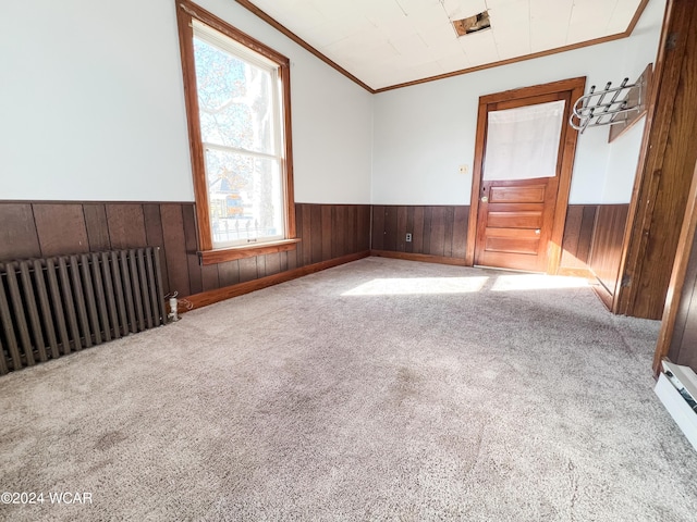 carpeted empty room featuring radiator, ornamental molding, baseboard heating, and wood walls