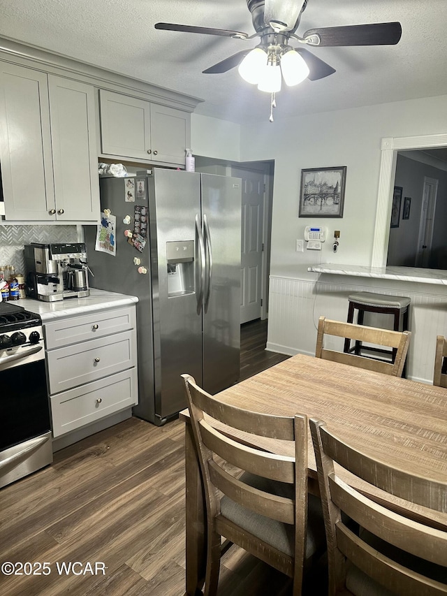kitchen featuring tasteful backsplash, dark wood-style flooring, gas range oven, ceiling fan, and stainless steel refrigerator with ice dispenser