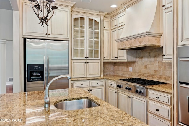 7 Estate Dr, Lima, OH 45805 - kitchen with appliances with stainless steel finishes, custom range hood, cream cabinetry, a sink, and light stone countertops